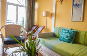 Wohnzimmer Couch mit grüner Auflage und Polster, weisser Sessel mit blauem Polster, zwei Liegestühle und eine Lampe im Hintergrund